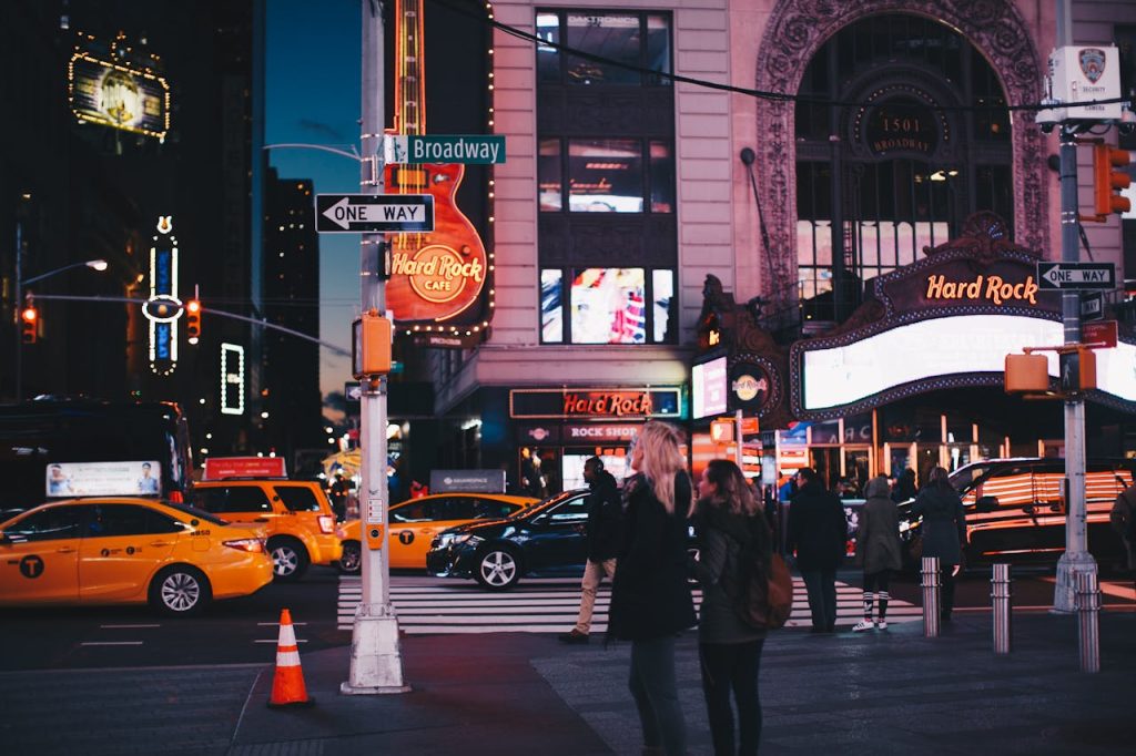 A bustling street view of Broadway at night featuring Hard Rock Cafe, taxis, and pedestrians in New York City.